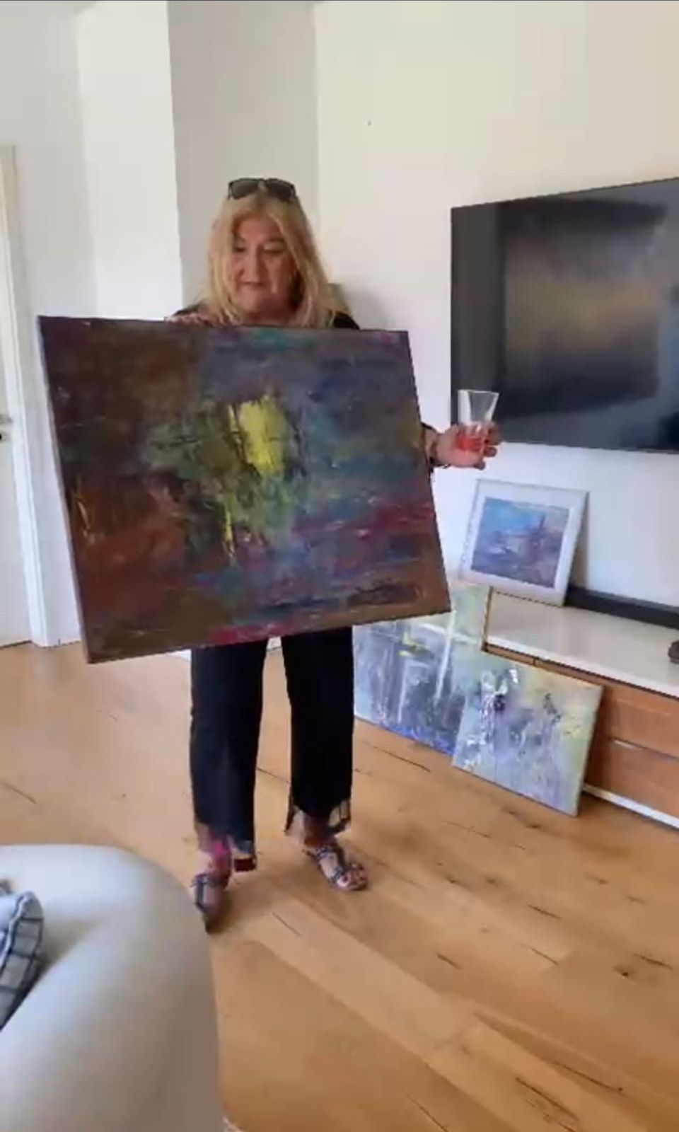Die Künstlerin hält ein großformatiges abstraktes Bild bei der Privatvernissage